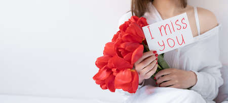 Bouquet of flowers in female hands, postcard I miss you on a white background. Isolated picture of a girl with tulips. Flower delivery concept. Bannerの写真素材