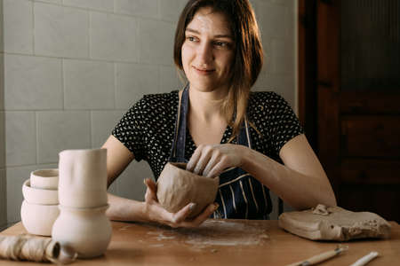 a beautiful woman potter sits at the table and makes a product from clay. the concept of rest and engaging in a favorite hobby.の写真素材