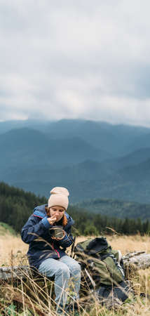 Girl tourist in the mountains eats the travelers special food, instant noodles in nature. traveler food concept. Horizontal banner.の写真素材