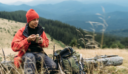 Tourist food in the mountains. Male traveler eating instant noodles looking at the mountain, positive emotions and a snack in natureの写真素材