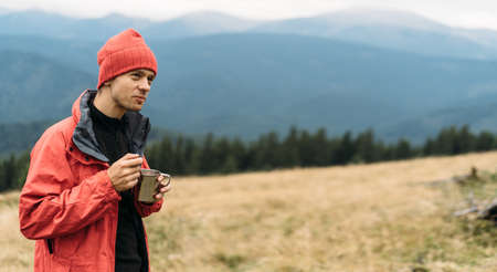 Portrait of caucasian tourist man eating fast food in the mountains, instant noodles for the traveler, delicious lunch in nature while relaxing.の写真素材