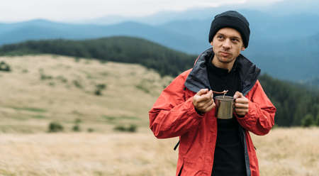 Portrait of caucasian tourist man eating fast food in the mountains, instant noodles for the traveler, delicious lunch in nature while relaxing.の写真素材