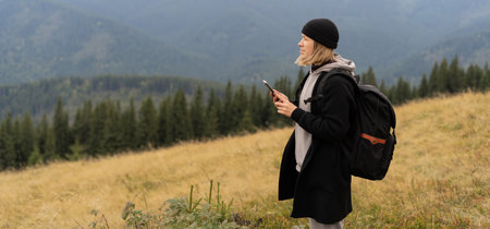 girl standing on top of a mountain using a mobile phone, tourist on a background of mountains with a smartphone, mockup for a text messageの写真素材