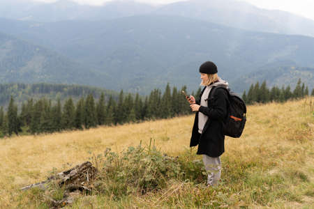 girl traveler in a hat while on vacation in nature and plans an online route map in a smartphone, a tourist girl uses a mobile phone enjoying her vacation against the backdrop of a mountain panorama.の写真素材