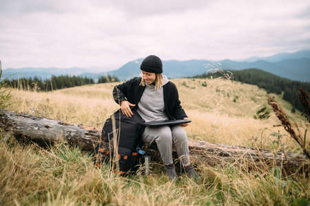 woman working with laptop sitting in the mountains. Caucasian lady takes a laptop out of her backpack while hiking in the highlands.の写真素材