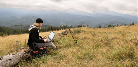 woman working with laptop sitting in the mountains. Tourist tourist enjoying the view of the valley. Holidays on an autumn day.の写真素材