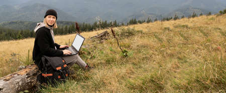 Caucasian woman working on her computer at the top of the mountain. Remote work concept. The traveler works remotely while enjoying the mountain landscape while on vacation.の写真素材