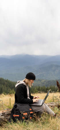 Caucasian woman working on her computer at the top of the mountain. Remote work concept.の写真素材