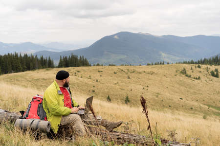 Man traveler using laptop, working at the top of the mountain. Remote work with a laptop. The man sits upstairs.の写真素材