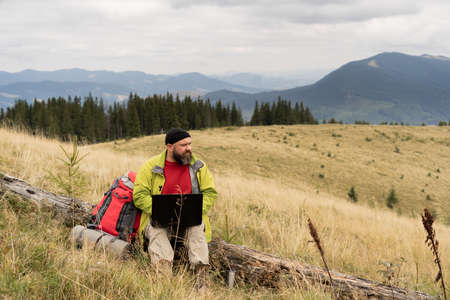 Caucasian bearded man working on his computer at the top of the mountain. Remote work concept.の写真素材
