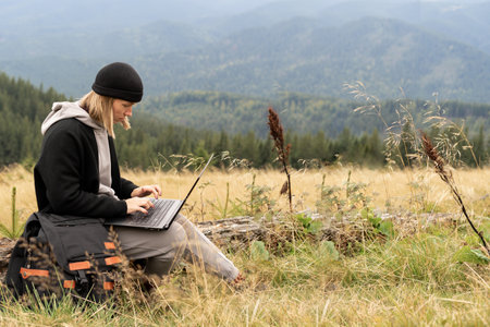 Caucasian woman working on her computer at the top of the mountain. Remote work concept. The traveler works remotely while enjoying the mountain landscape while on vacation.の写真素材