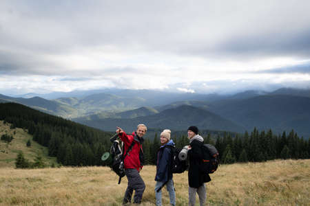 Hiking in the mountains, friends travelers looking forward, view of mountains and cloudy sky, people active lifestyle in the alps, mountain tourismの写真素材