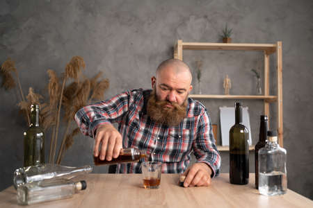 bearded millennial alcoholic man drinking whiskey at home. Alcohol addiction. Treatment of alcoholism.の写真素材