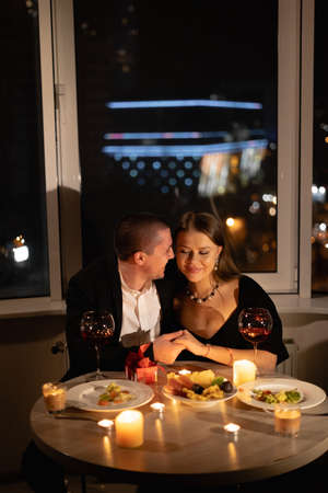 couple in love for valentines day, candlelight dinner, red wine on a date, a man holding a womans hand at a festive table, love and romanceの写真素材