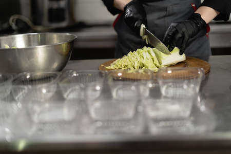 takeaway food in the restaurant. Close-up of a chefs hands in gloves preparing a cabbage salad. Disposable lunch boxes are on the table. Food delivery.の写真素材