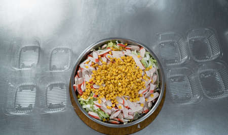 takeaway food in the restaurant. Close-up of a large bowl with salad of corn and crab sticks with cabbage stands on the table near disposable plastic trays. Food delivery.の写真素材