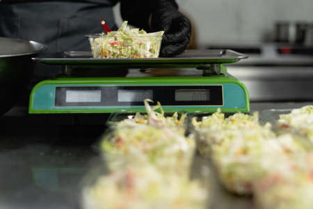 food delivery in the restaurant. Close-up of a chefs hand in gloves weighing a portion of salad on an electronic scale. Small business. Takeout food.の写真素材