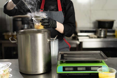 Food delivery. In the restaurant, the chef prepares food and prepares it in disposable dishes. closeup female hands pour broth with sausages into lunch boxes.の写真素材