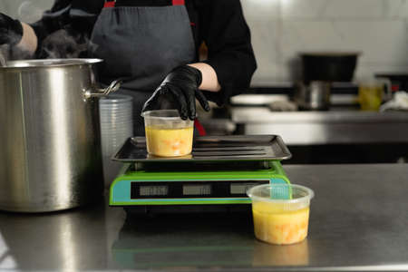 Food delivery. In the restaurant, the chef prepares food and prepares it in disposable dishes. closeup female hands pour broth with sausages into lunch boxes.の写真素材