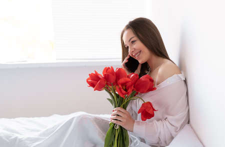 Portrait of a sexy girl with a bouquet of red tulips in the morning in the bedroom for Valentines Day. Woman with flowers on the bed Womens dayの写真素材