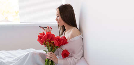 Portrait of a sexy girl with a bouquet of red tulips in the morning in the bedroom for Valentines Day. Woman with flowers on the bed Womens dayの写真素材