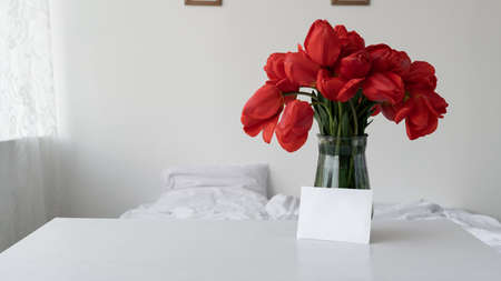 Womens holiday background vase with red flowers. Morning tulips in the bedroom. Birthday or mothers day bouquet of flowers. Women holidayの写真素材