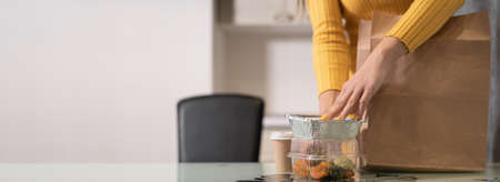 Close-up of female hands take out food in disposable trays from a paper bag and put it on the table. Without a face. Baner. copy space.の写真素材