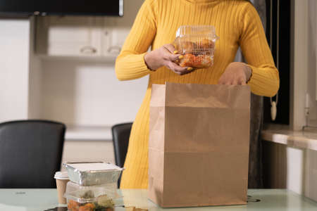 Close-up of female hands take out food in disposable trays from a paper bag and put it on the table. Without a face. Baner.の写真素材