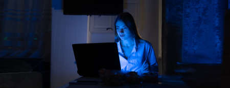 Attractive young woman working at home at night using a laptop in casual clothes. Baner. copy space.の写真素材