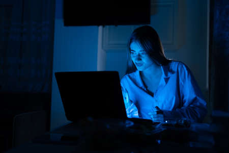 Uncertain in bewilderment, a girl makes a questioning gesture, has an ignorant and bewildered look, a lady in the evening at home at her laptop works remotely or watches a movie.の写真素材
