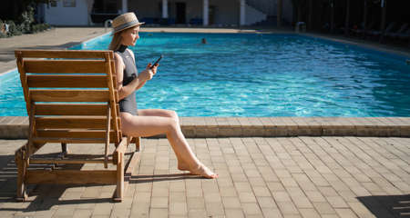 Summer day life women relaxing next to the luxury sunbathing pool on the beach of the outdoor hotel resort. sitting on a sun lounger with a smartphone. Summer concept. Baner.の写真素材