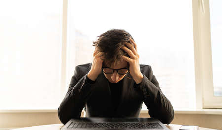 Depressed businessman with headache in the office. Business executive with migraine. hands on the head of a freelancer at the workplace. Office worker health conceptの写真素材