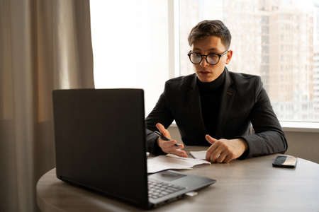 Young man, businessman sitting at the workplace in the office with a laptop, online work and education, online store sales, video communication with colleaguesの写真素材