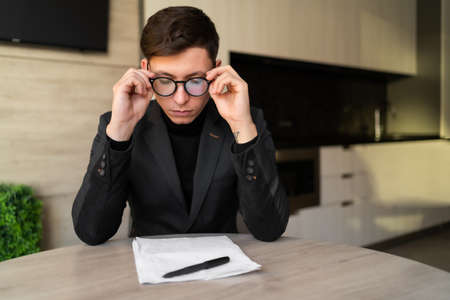 Health problem concept. Decreased vision of a man with glasses, headache of an office employee, businessman pain in his eyes, work at home fatigue.の写真素材