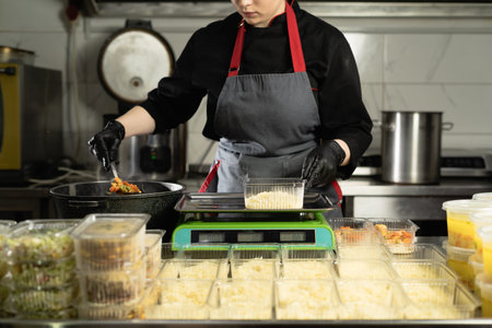 food delivery in the restaurant. hands of a woman chef in uniform with gloves weighing a portion of...