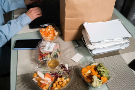 Office worker with smartphone having lunch at the workplace, close-up. Online food ordering. disposable tableware with vegetables. Food deliveryの写真素材