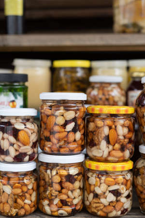 Various nuts in honey. A stand with products in the street market. Cashews, walnuts, almonds, hazelnuts and other nuts in honey or syrup in jars.の写真素材