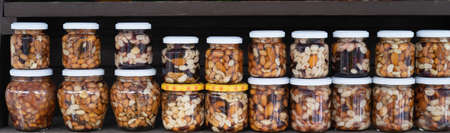 Various nuts in honey. A stand with products in the street market. Cashews, walnuts, almonds, hazelnuts and other nuts in honey or syrup in jars.の写真素材