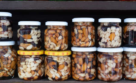 Various nuts in honey. A stand with products in the street market. Cashews, walnuts, almonds, hazelnuts and other nuts in honey or syrup in jars.の写真素材