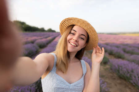 outdoors romantic portrait of young happy and attractive woman in white summer dress taking selfie with mobile phone on beautiful lavender flowers fieldの写真素材