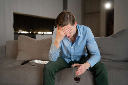 Male depression. Upset caucasian man has problems sitting at home on the sofa and thinking, bad thoughts, breaking up with lover, financial difficulties concept, copy spaceの写真素材