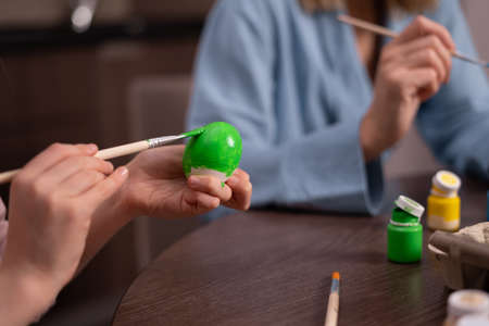 Hands paint Easter eggs in a modern style with green paint. creativity with children, traditional symbols. Preparation for Easter.の写真素材