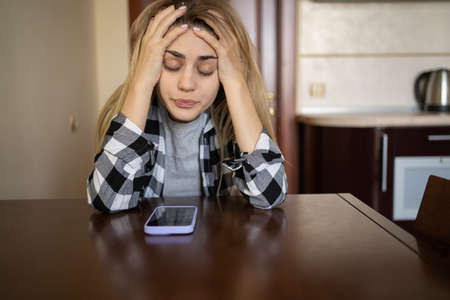 Lonely sad girl in depression is waiting for a phone call, sitting at the table at home. depressed. copyspace.の写真素材