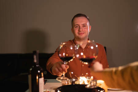 Celebrating valentines day concept. Portrait of handsome man with glass of red wine, romantic dinner for two, toast and clinking glassesの写真素材