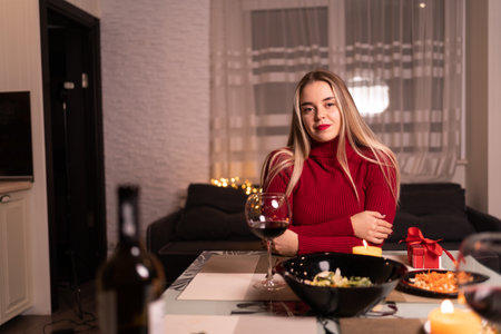 young lady lonely having dinner at home with wine, dating online valentines day, woman with wine glass alone at table with food and alcoholの写真素材