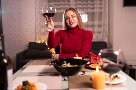 Beautiful woman at home romantic dinner, wine glass of red, online date on webcam, celebration of valentines day, single birthdayの写真素材