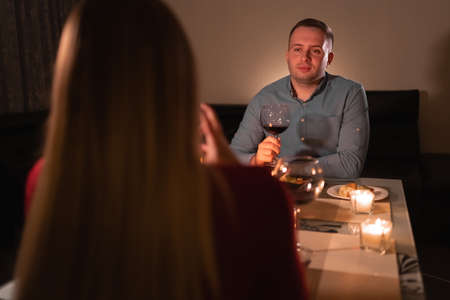Happy young couple in love drinking wine, romantic date, celebrate lovers valentine's day, man and woman dinner with candles at home sitting at table, valentine's day or birthday celebration conceptの写真素材