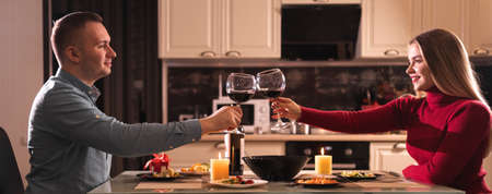 A couple in love on valentines day have dinner at home and drink red wine in glasses. Alcohol at dinner for two. Date of a man and a woman.の写真素材