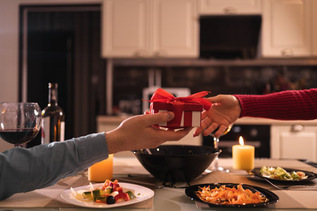 Valentines day date couple, romance and lovers gift, holding surprise gift with hands, dinner for two with wine and candles, no facesの写真素材