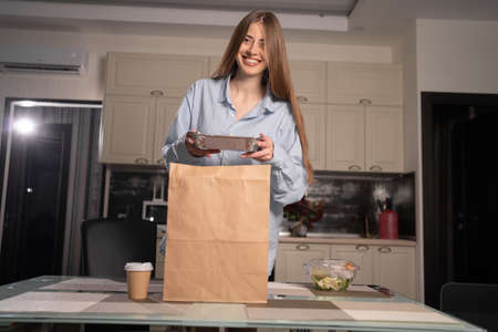 Caucasian woman unpacking online food home delivery, disposable tableware with salad for lunch, housewife keto diet and weight loss, restaurant or cafe food delivery serviceの写真素材